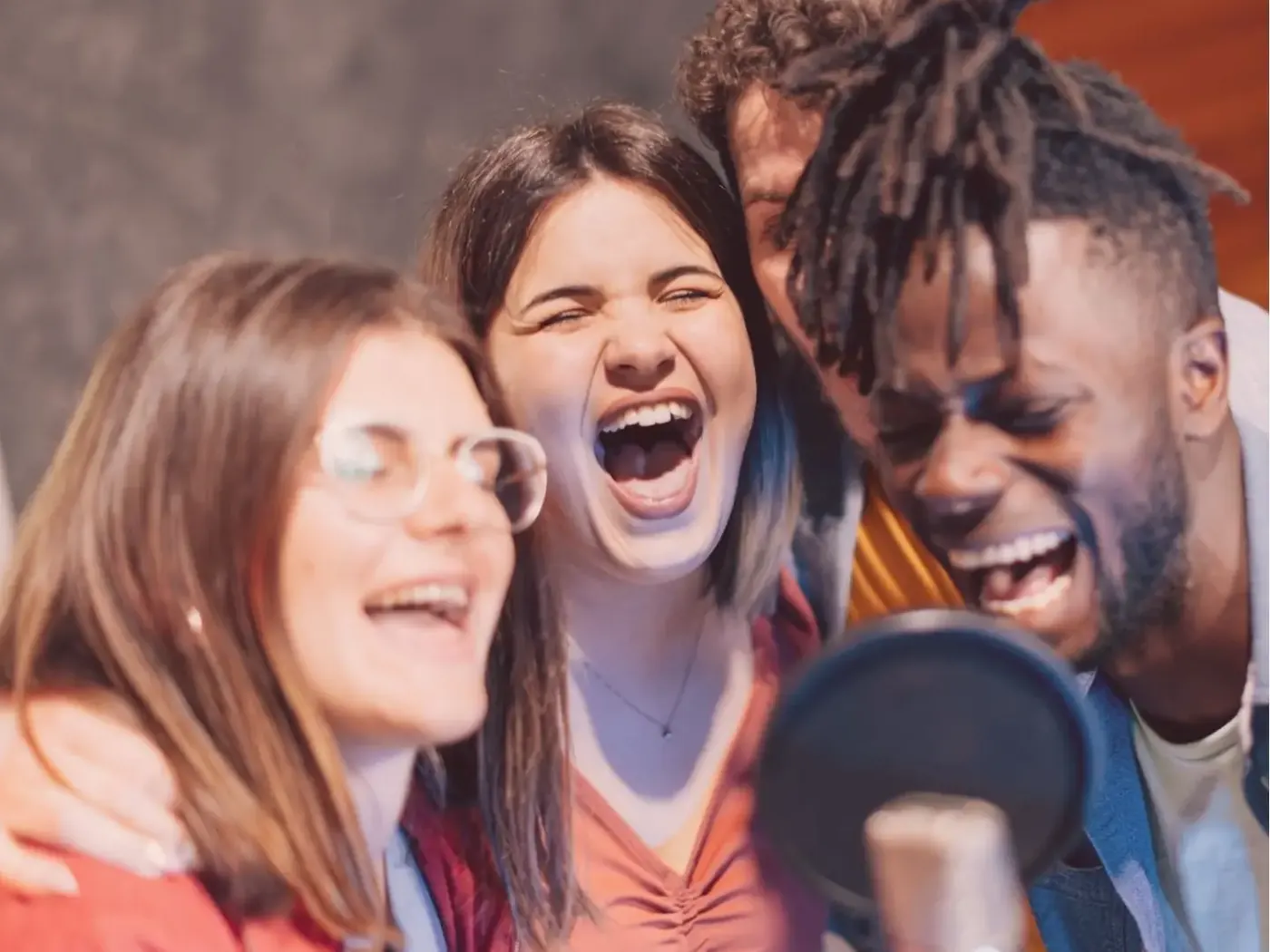 Üç arkadaş gülerek birlikte mikrofona şarkı söylüyor: Music Campus Bielefeld'de karaoke gecesi